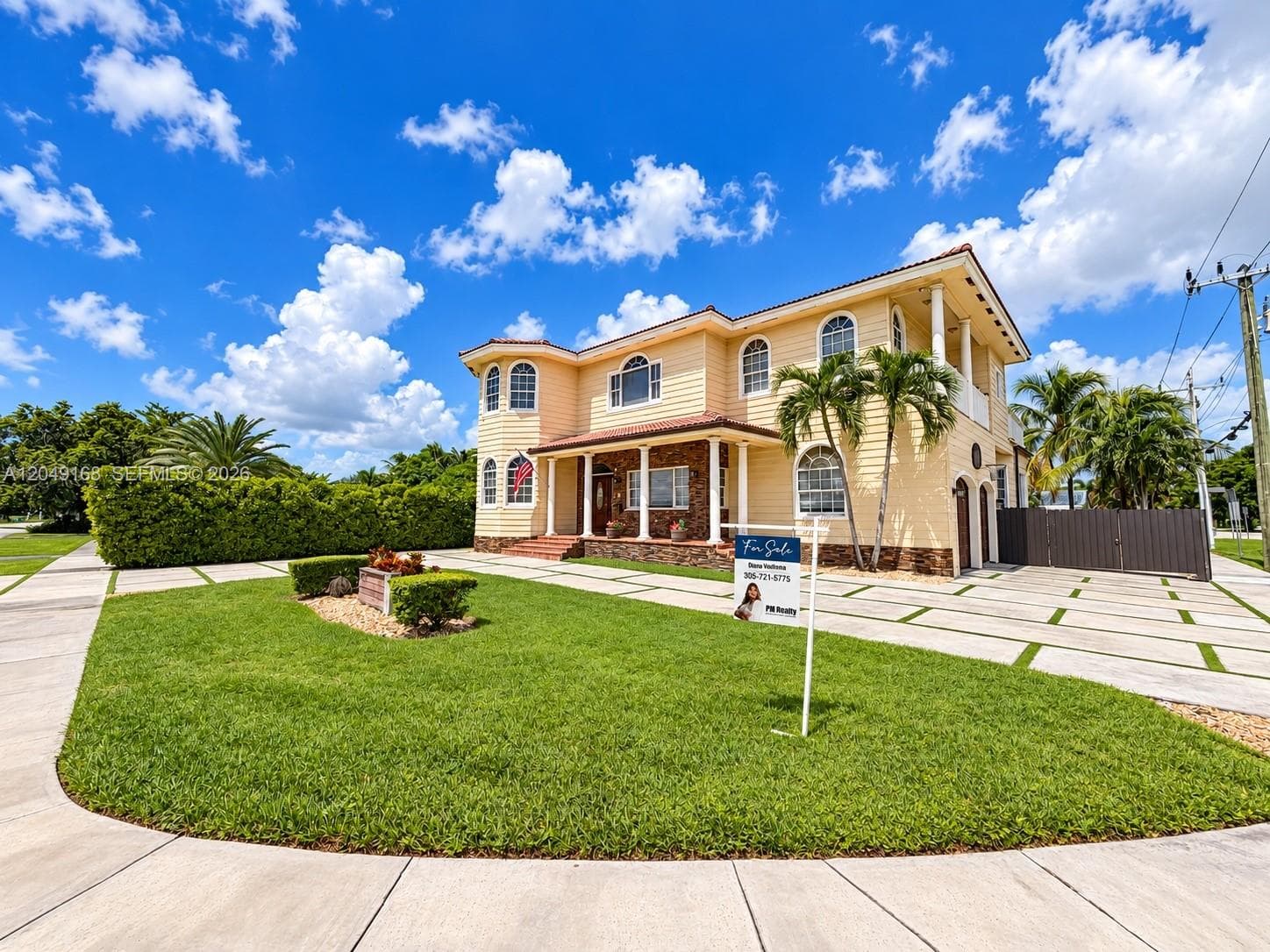 Two-story residence featuring light-colored horizontal siding, stone veneer accents, arched windows, covered porch with classical columns, and a paved driveway with integrated lawn grid