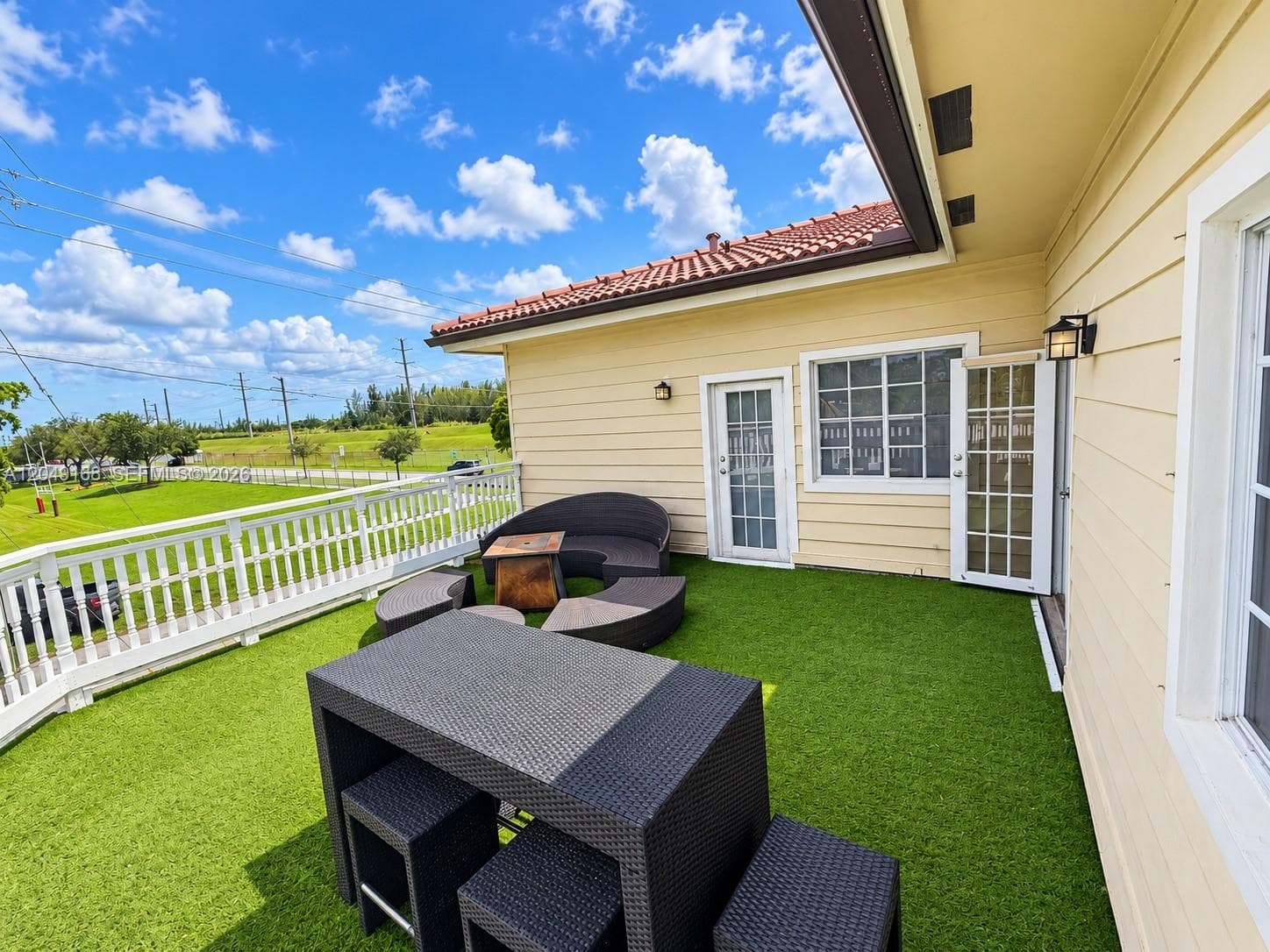 Elevated exterior deck featuring synthetic turf flooring, white spindle railings, and exterior wall-mounted lighting