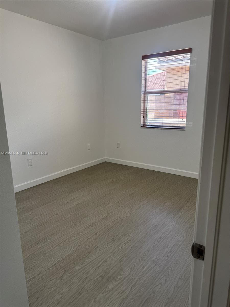 Neutral-toned wood-finish flooring, crisp white walls, and a single-pane window with wood-finish horizontal blinds