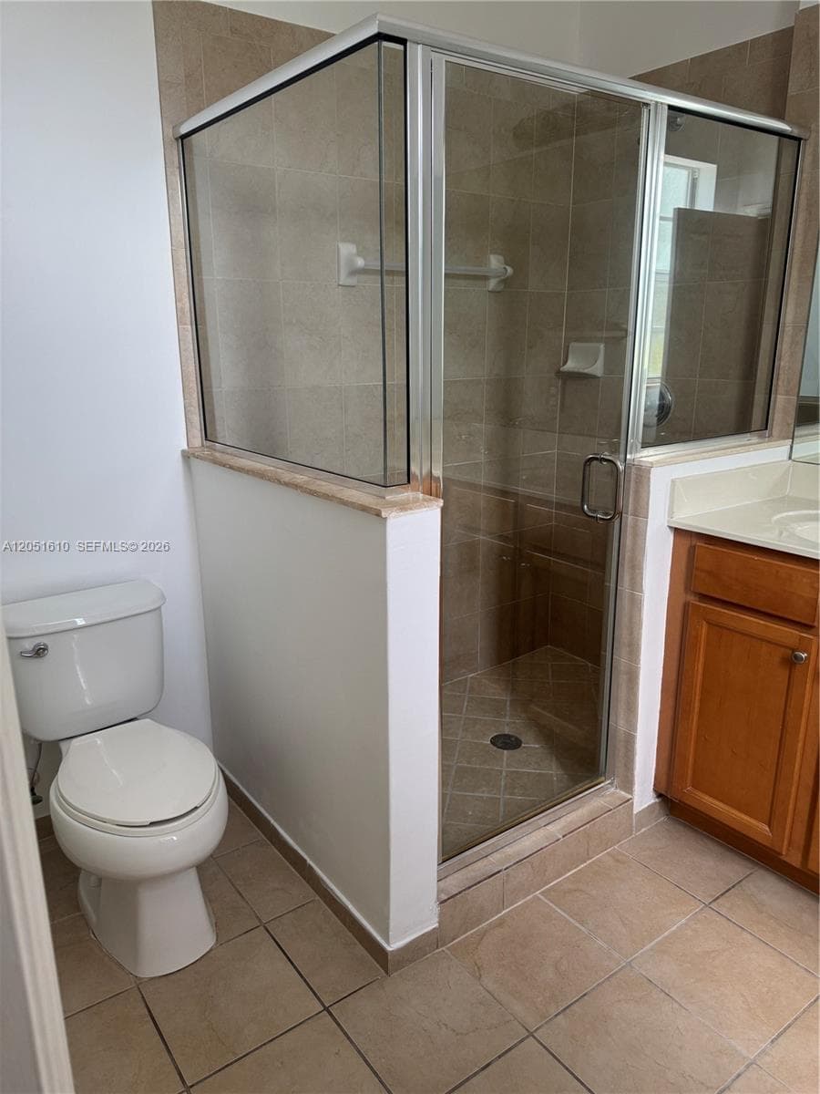 Enclosed shower featuring a glass door and stone tile surround, complemented by a wood-finish vanity with a solid-surface countertop and ceramic tile flooring