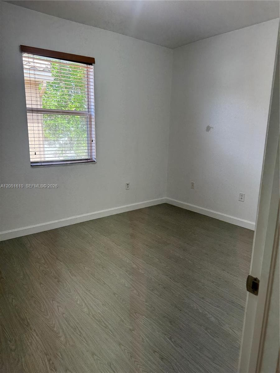 Room featuring wood-finish flooring, neutral walls, and a single-pane window with horizontal blinds and a wooden valance