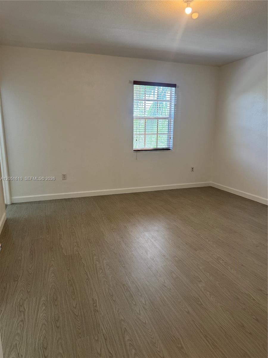 Neutral-toned interior space featuring wood-finish flooring, a single-pane window with horizontal blinds, and overhead lighting