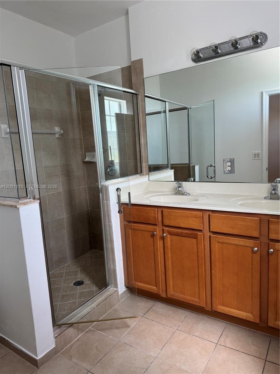 Double vanity featuring wood cabinetry, solid surface countertop with dual drop-in sinks, full-width mirror, and a walk-in shower with tiled surround and glass enclosure