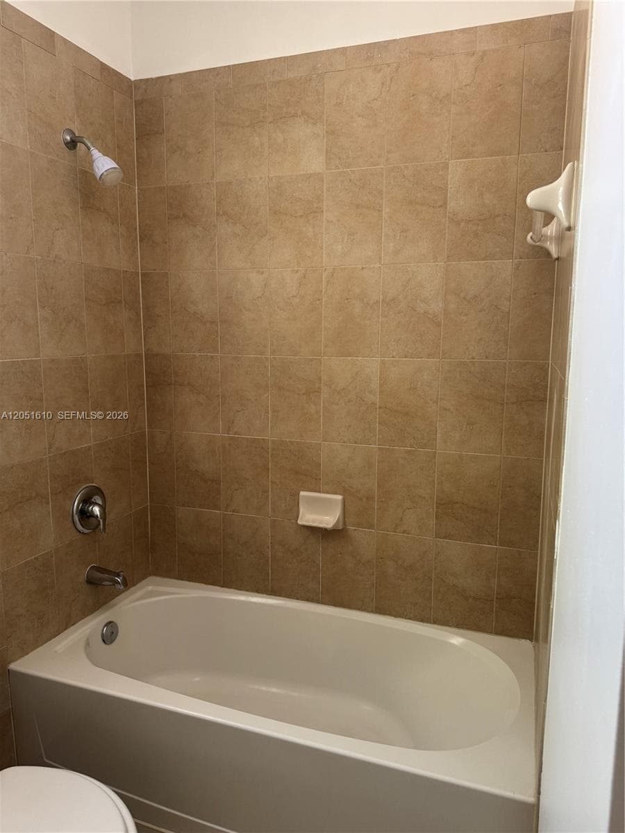 Full-size soaking tub featuring a neutral-toned tile surround, integrated soap dish, and polished chrome shower fixture