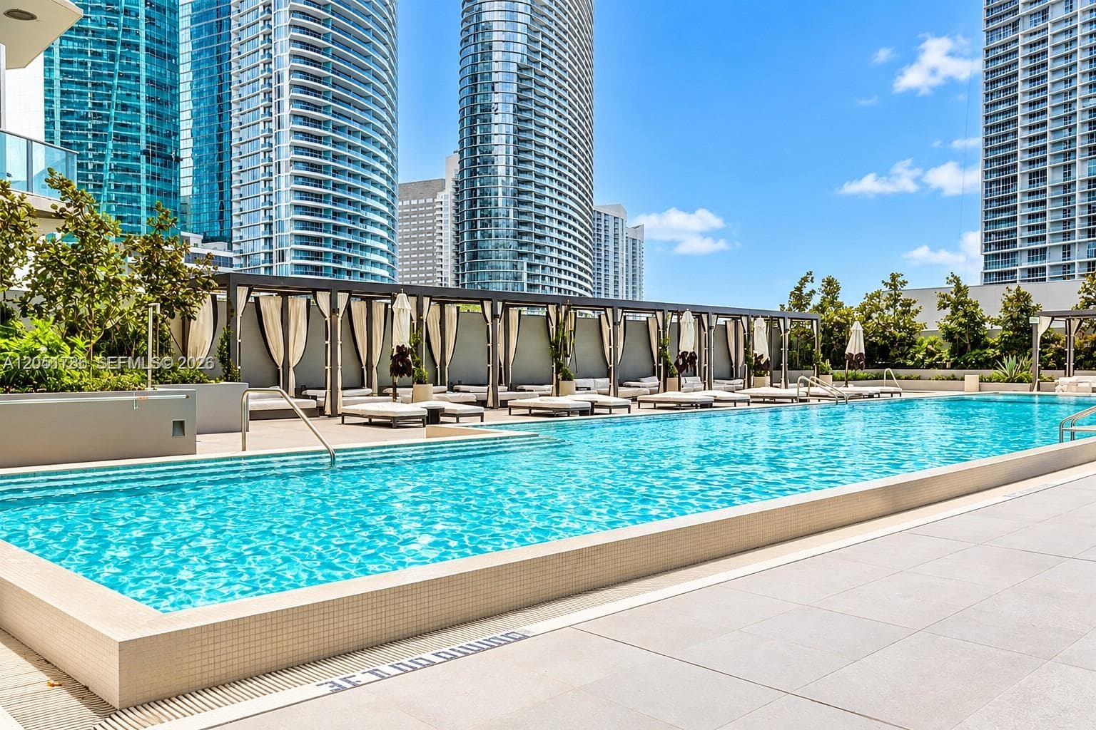 Swimming pool with a tiled perimeter, expansive sun deck featuring large-format stone pavers, and a structural pergola