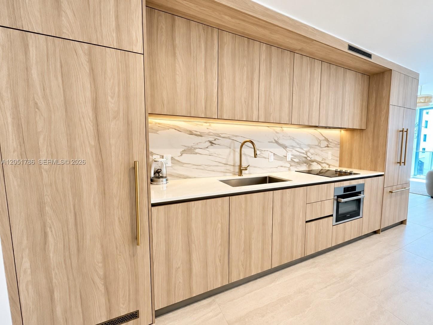 Custom wood-finish cabinetry featuring integrated appliances, solid-surface countertops, stone-patterned backsplash, and gold-tone hardware