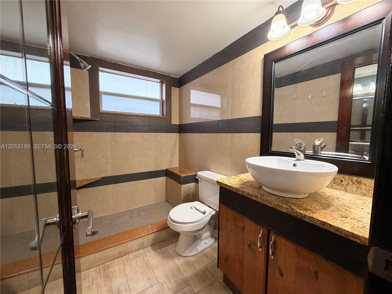 Bathroom featuring a stone-finish countertop, white vessel sink, wood-finish cabinetry, and tiled walk-in shower with built-in corner shelving