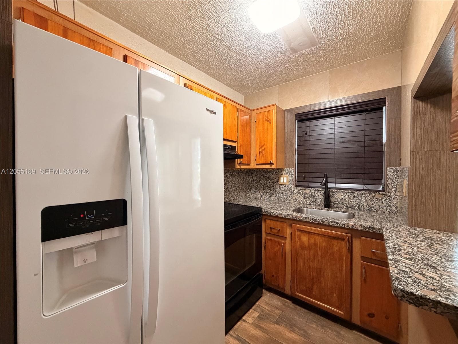 Kitchen featuring wood cabinetry, stone-surface countertops, wood-finish flooring, and a stainless steel undermount sink with a matte black faucet