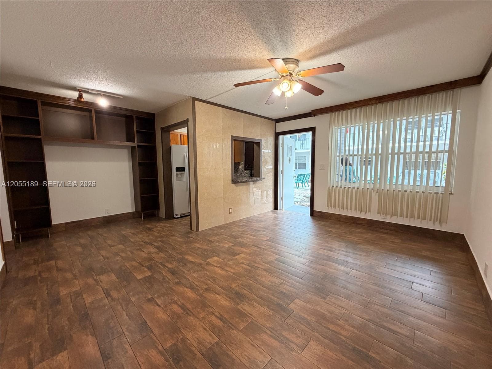 Wood-finish flooring, floor-to-ceiling built-in shelving, integrated ceiling fan with light fixture, and pass-through window with solid-surface ledge