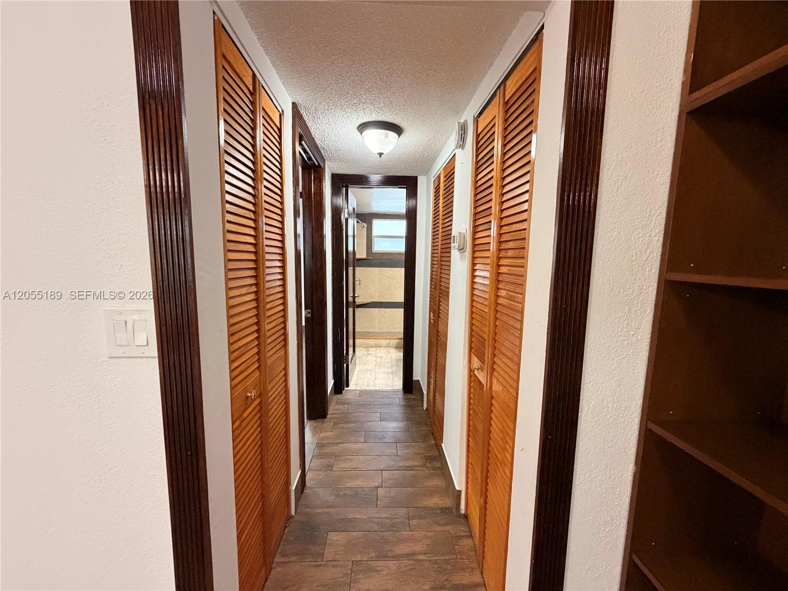 Hallway featuring wood-finish tile flooring, louvered closet doors, built-in shelving, and dark-stained door casing