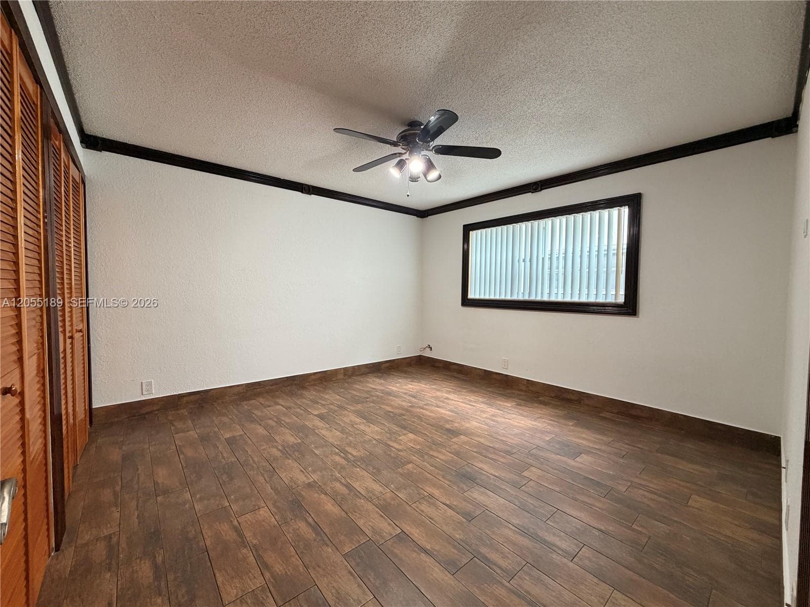 Room featuring wood-finish flooring, dark-trimmed crown molding, louvered bi-fold closet doors, a horizontal window, and a ceiling fan with integrated light fixture