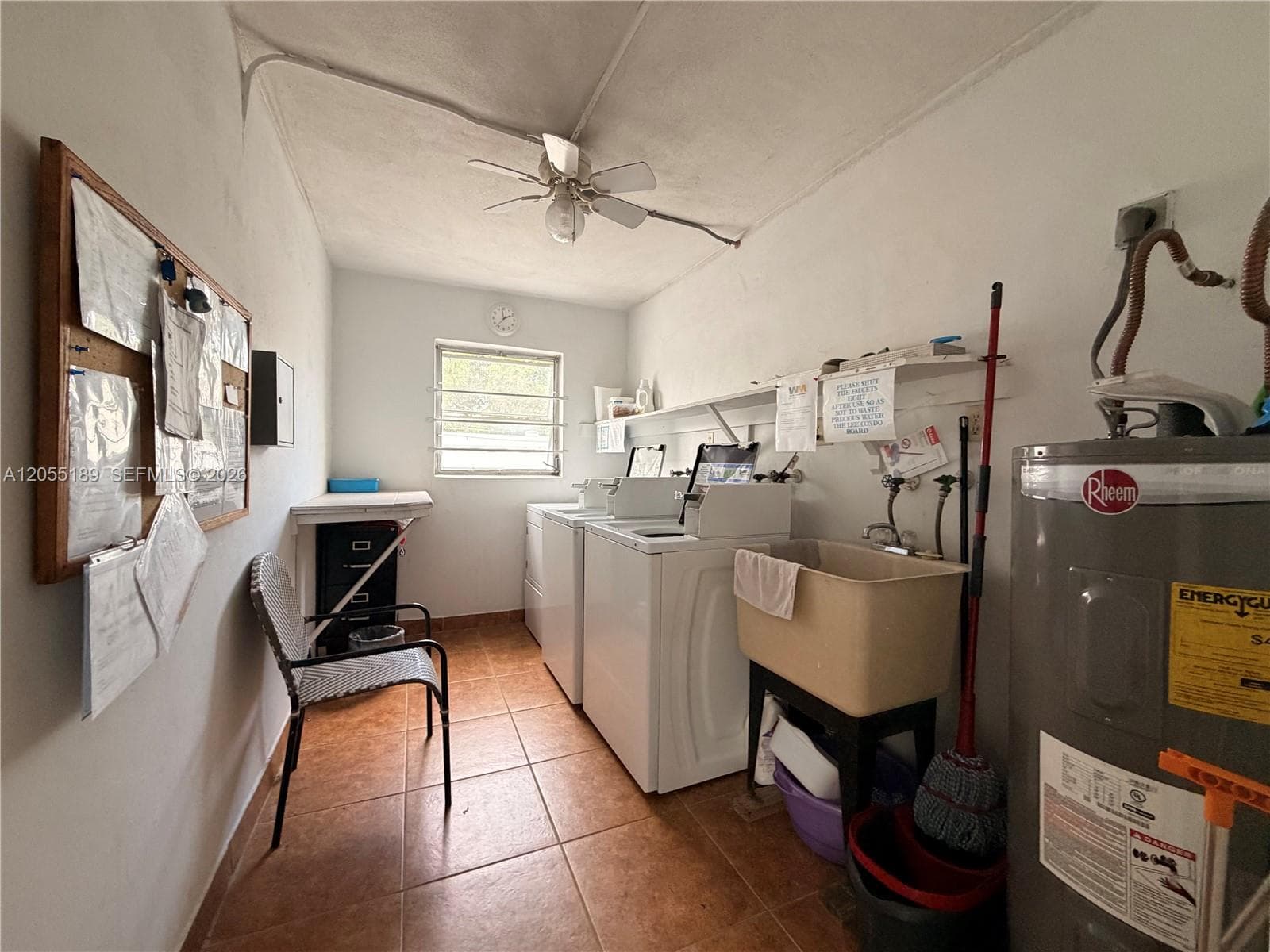 Utility area featuring ceramic tile flooring, a wall-mounted storage shelf, a basin sink, and a ceiling-mounted fan