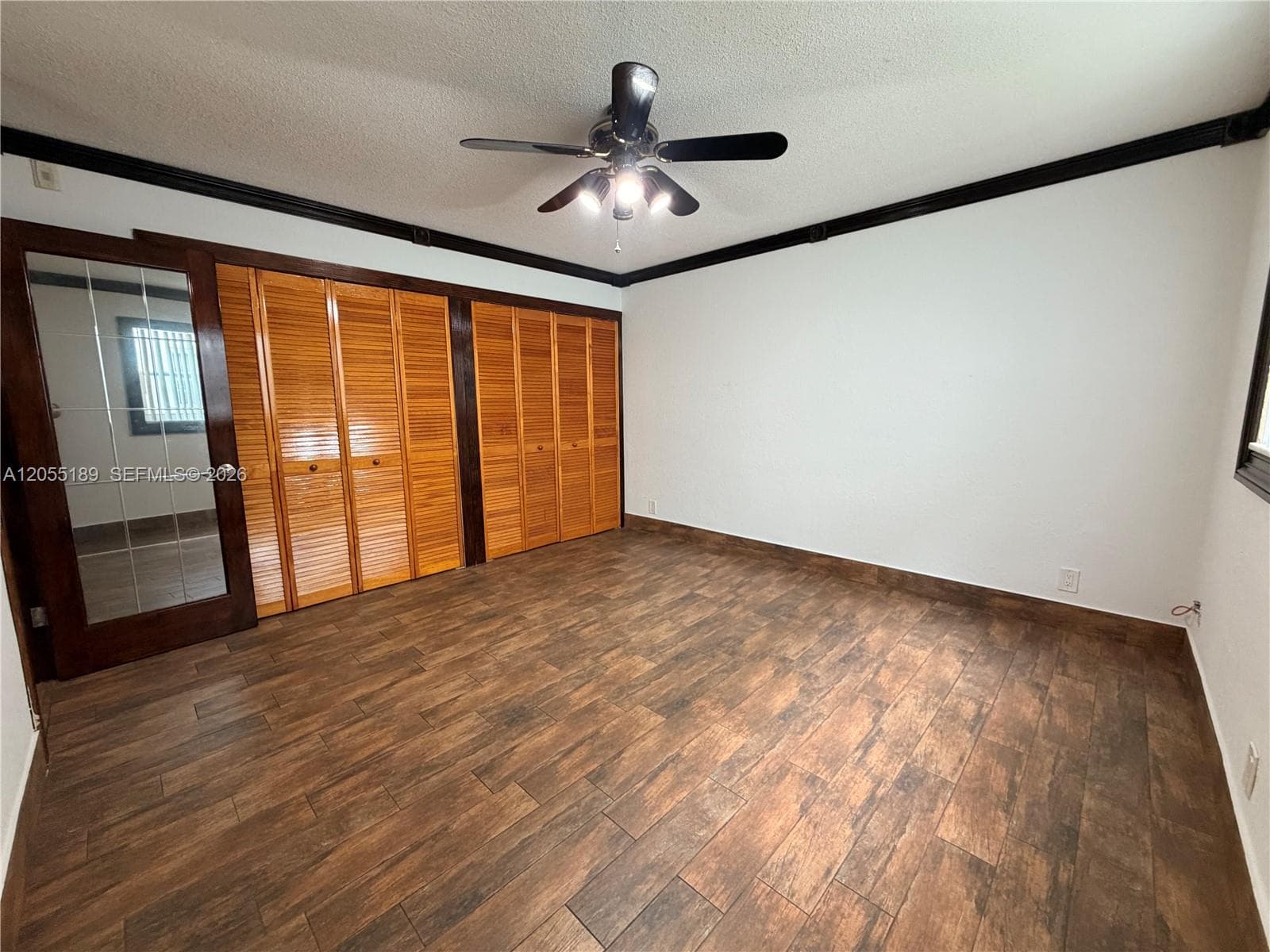 Room featuring wood-finish flooring, dark crown molding, louvered closet doors, a multi-pane glass door, and a central ceiling fan with integrated lighting
