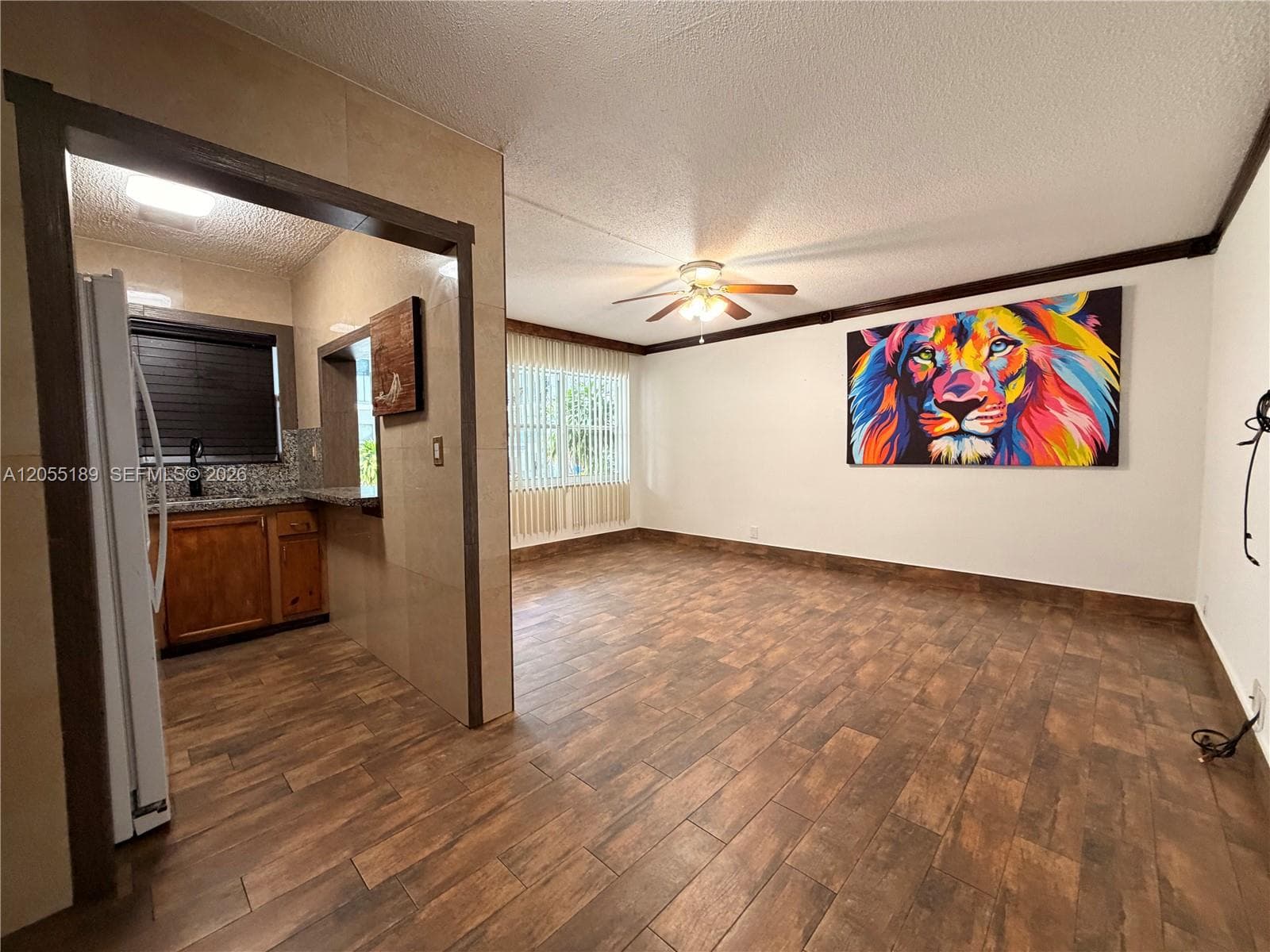 Wood-finish flooring throughout, tile-accented walls, ceiling-mounted fan, vertical window blinds, and wood-finish cabinetry
