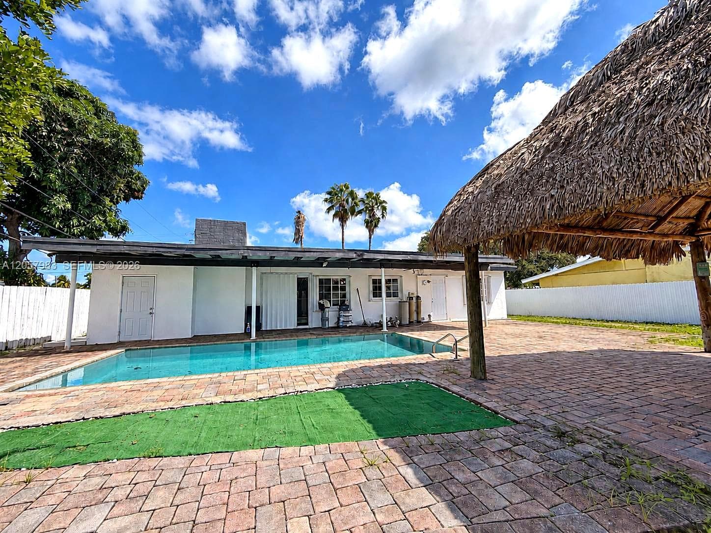Swimming pool with paver decking, adjacent to a thatched-roof structure