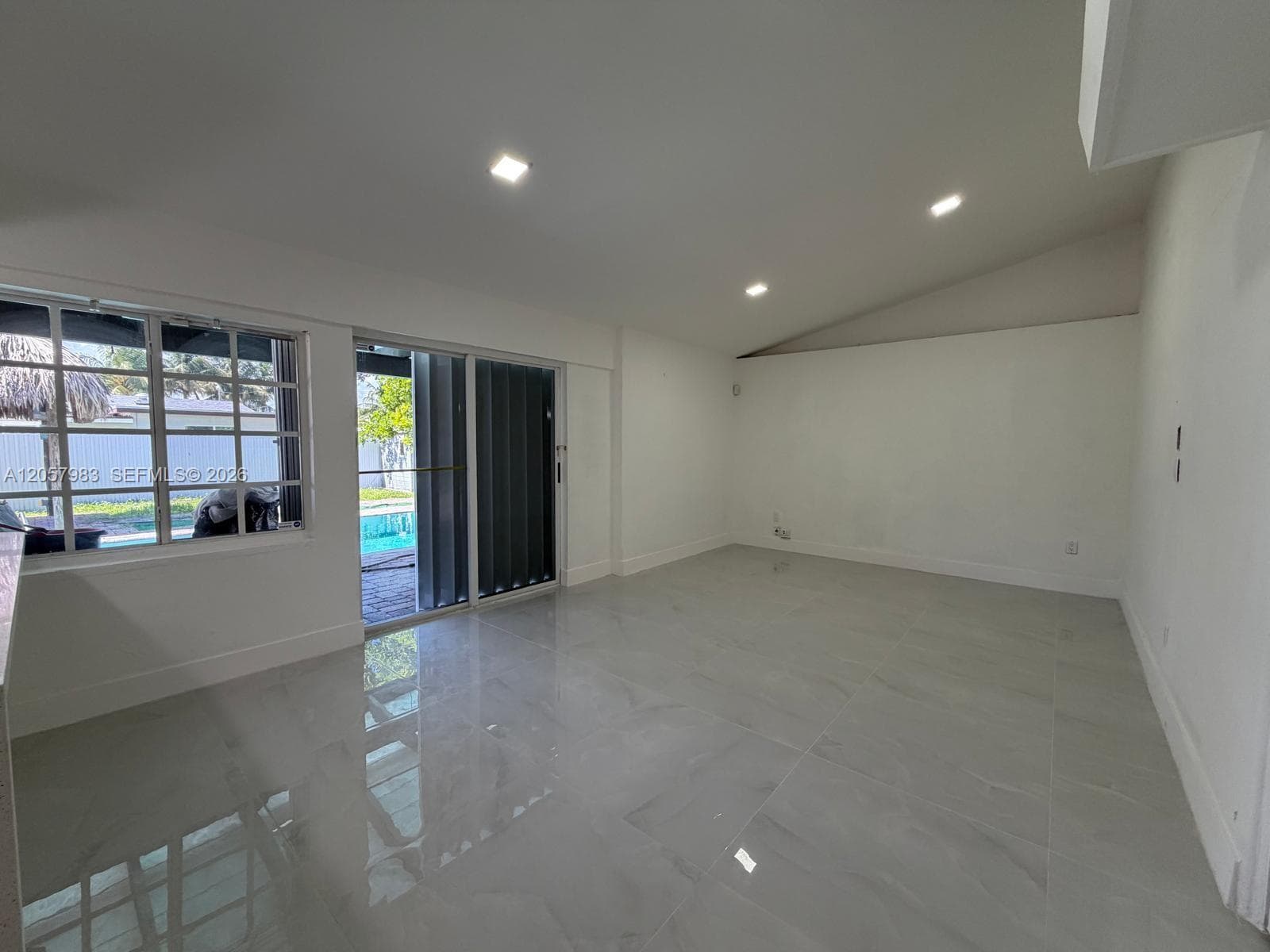 Recessed ceiling lighting, vaulted ceiling, large format tile flooring, sliding glass door, and a multi-pane window