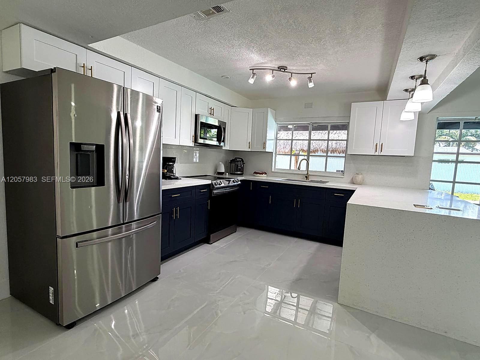 Modern kitchen with glossy tile flooring, stainless steel appliances, two-tone cabinetry, and light-colored countertops