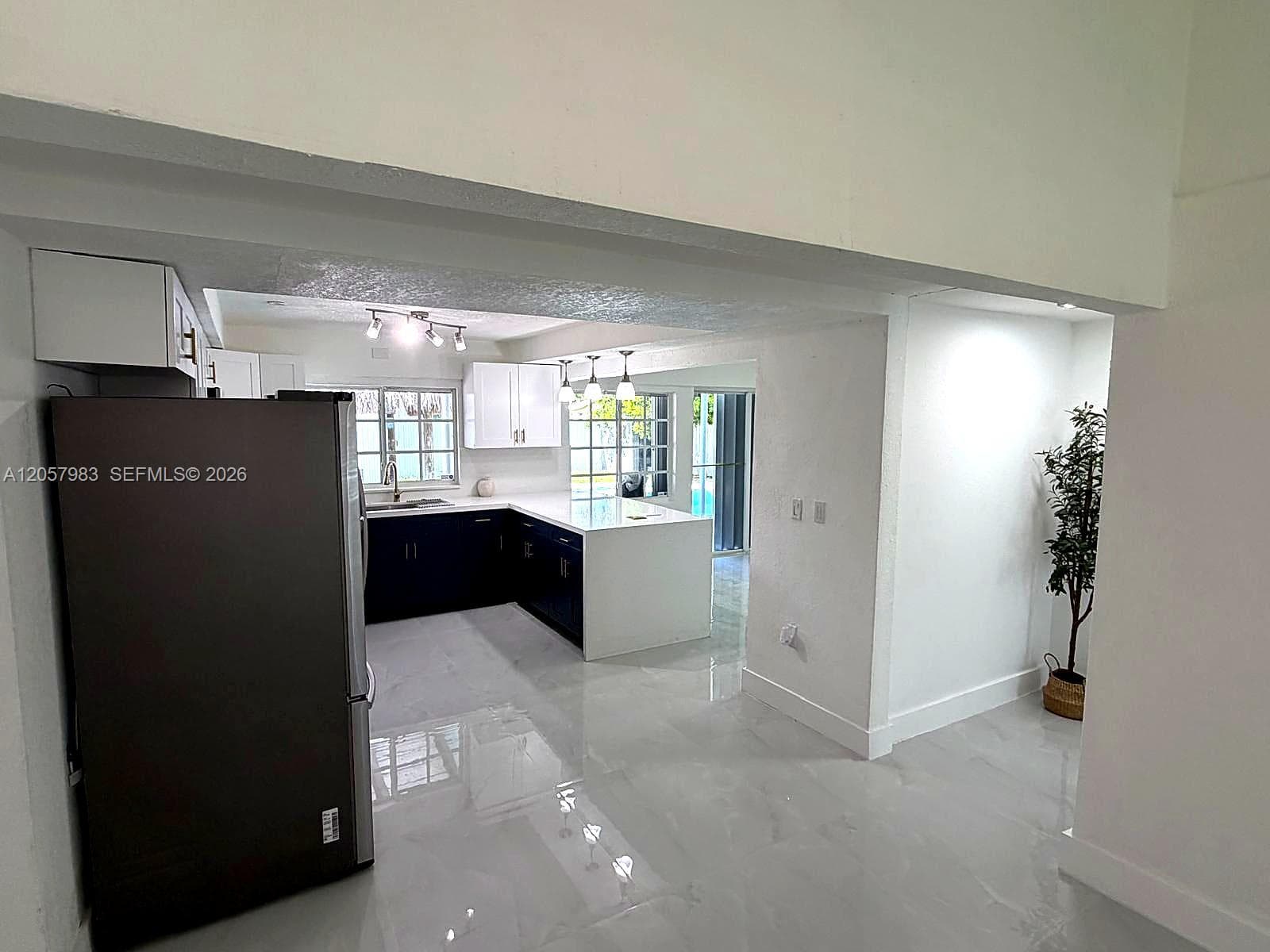 Modern kitchen with white upper and dark lower cabinetry, white countertops, and a full-size stainless steel refrigerator