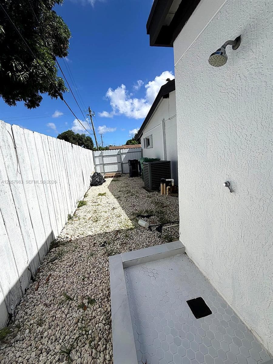 Outdoor shower with a rain-style shower head, white hexagonal tile flooring, and textured stucco wall