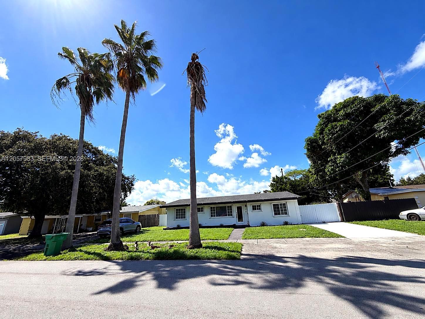 White exterior with a dark roof, a concrete driveway, and a white privacy fence