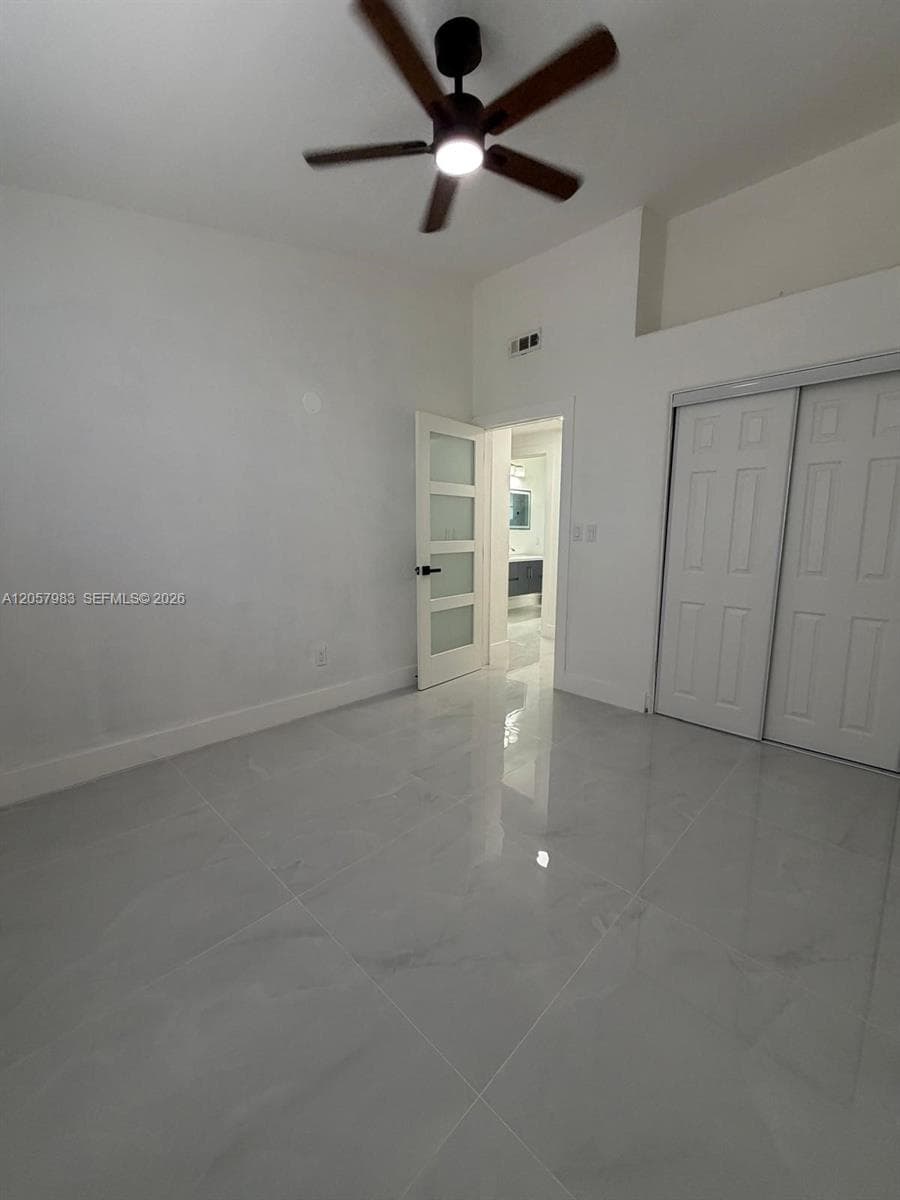 Polished tile flooring, ceiling fan, white walls, and white sliding closet doors