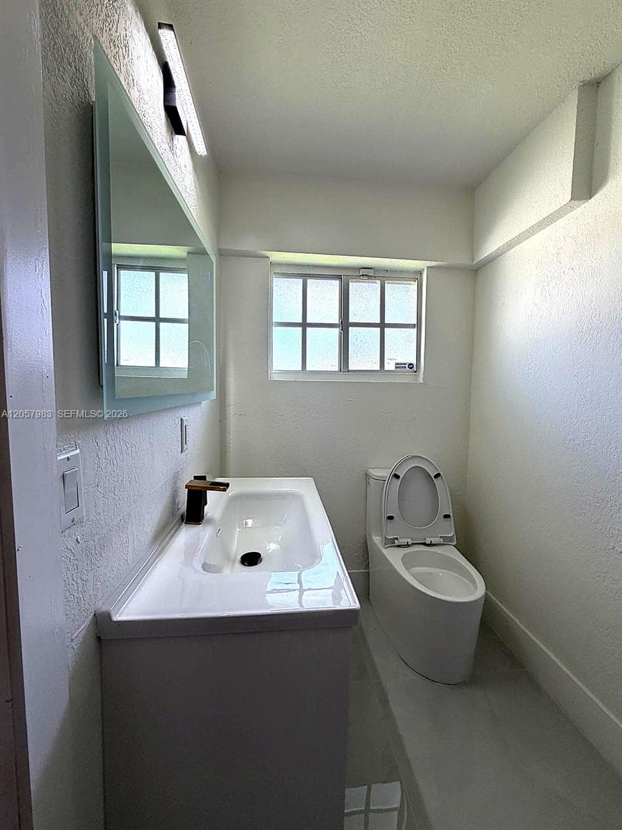 Contemporary vanity with integrated sink, black bronze single-handle faucet, illuminated mirror, and a modern toilet