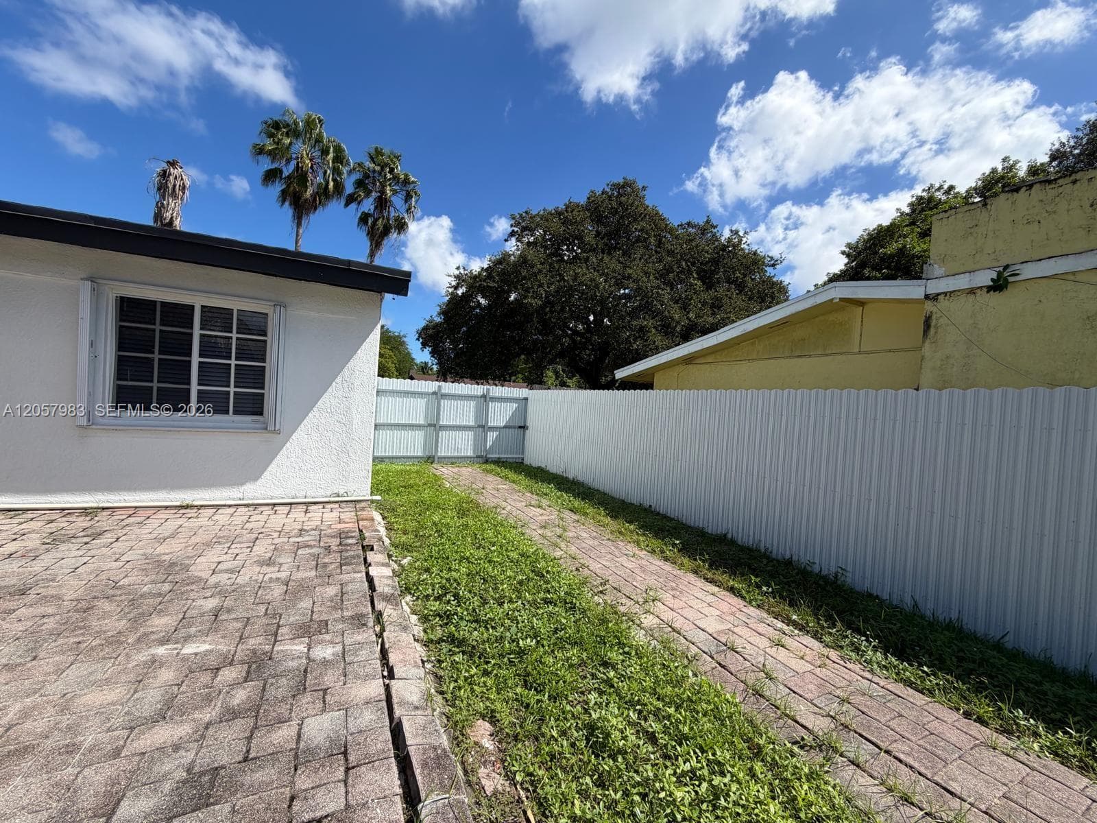 Paved side yard patio with a privacy fence and gate, featuring mature palm trees