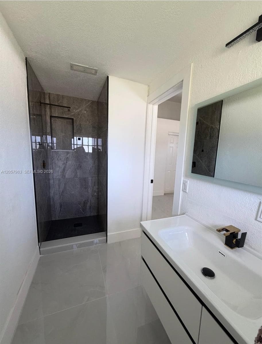 Glass-enclosed shower with dark-toned tile surround, light gray tile flooring, and a floating vanity with an integrated sink