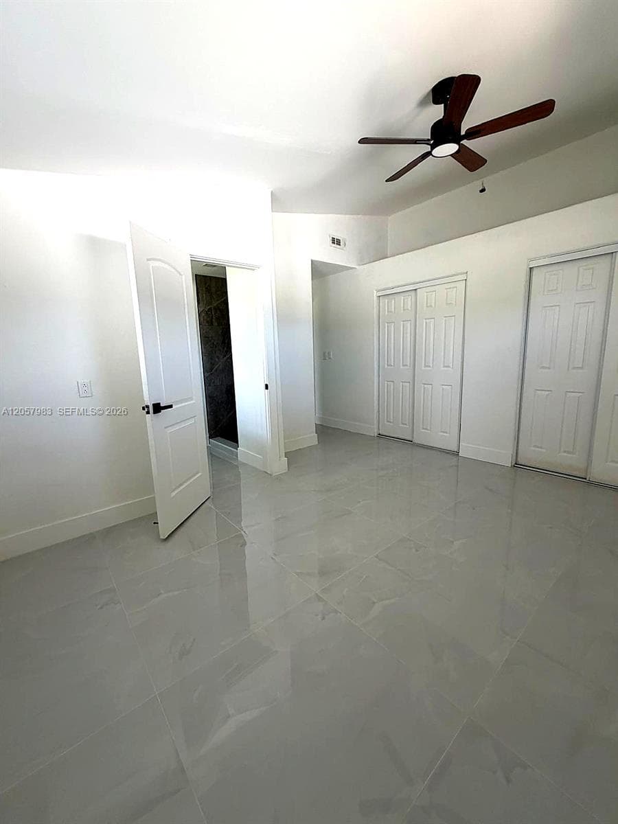 Spacious room featuring light-toned tile flooring, a dark-toned ceiling fan, and white doors with dark hardware