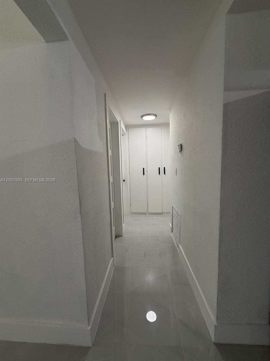 Hallway featuring a flush-mount ceiling light, white paneled doors, and glossy tile flooring