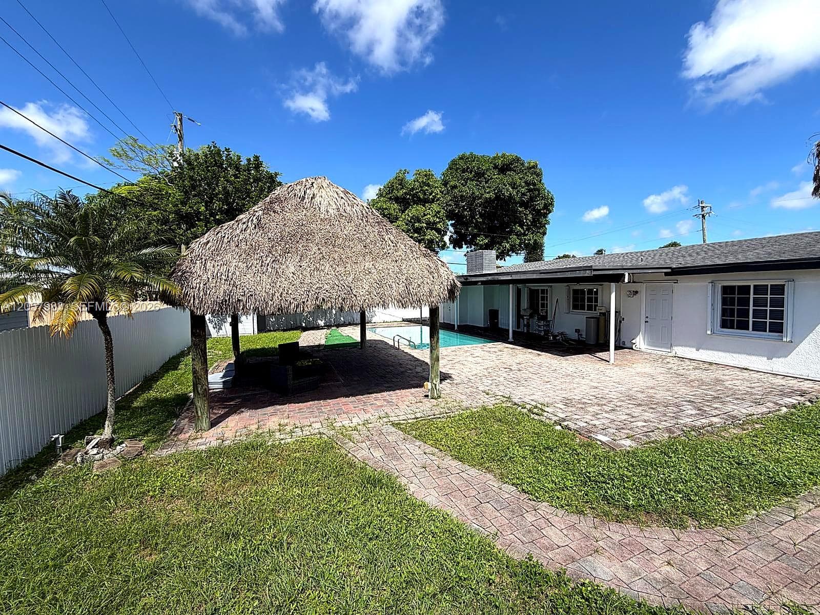 Private backyard featuring a thatched-roof tiki hut, brick paver patio, in-ground swimming pool, and white exterior