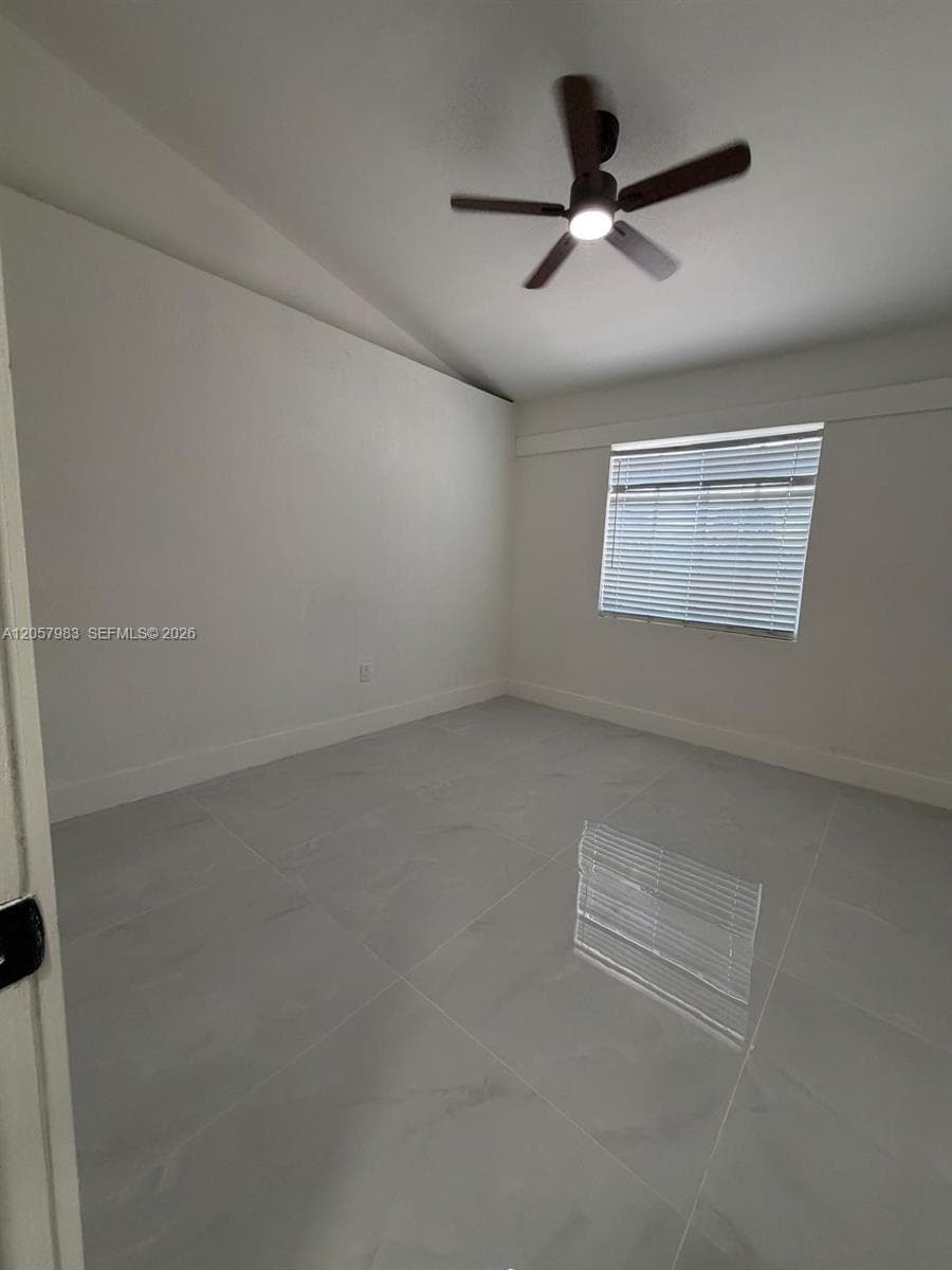 Vaulted ceiling, ceiling fan with integrated lighting, large format tile flooring, window with horizontal blinds, and white baseboards