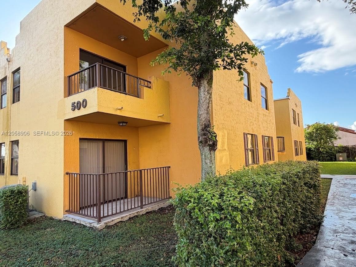 Stucco exterior featuring dual-level outdoor spaces with metal railings, sliding glass doors, and manicured landscaping