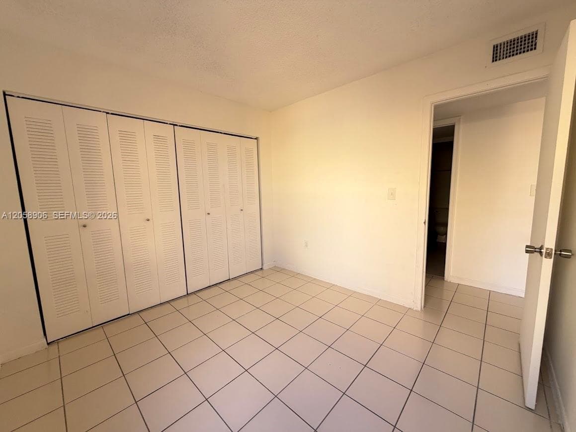 Interior room featuring white tile flooring and floor-to-ceiling closets with white louvered bifold doors