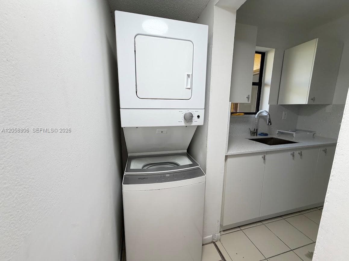 Stacked laundry unit featuring a top-load washer, white flat-panel cabinetry, a light-toned countertop, a single-basin sink with a chrome faucet, and tile flooring