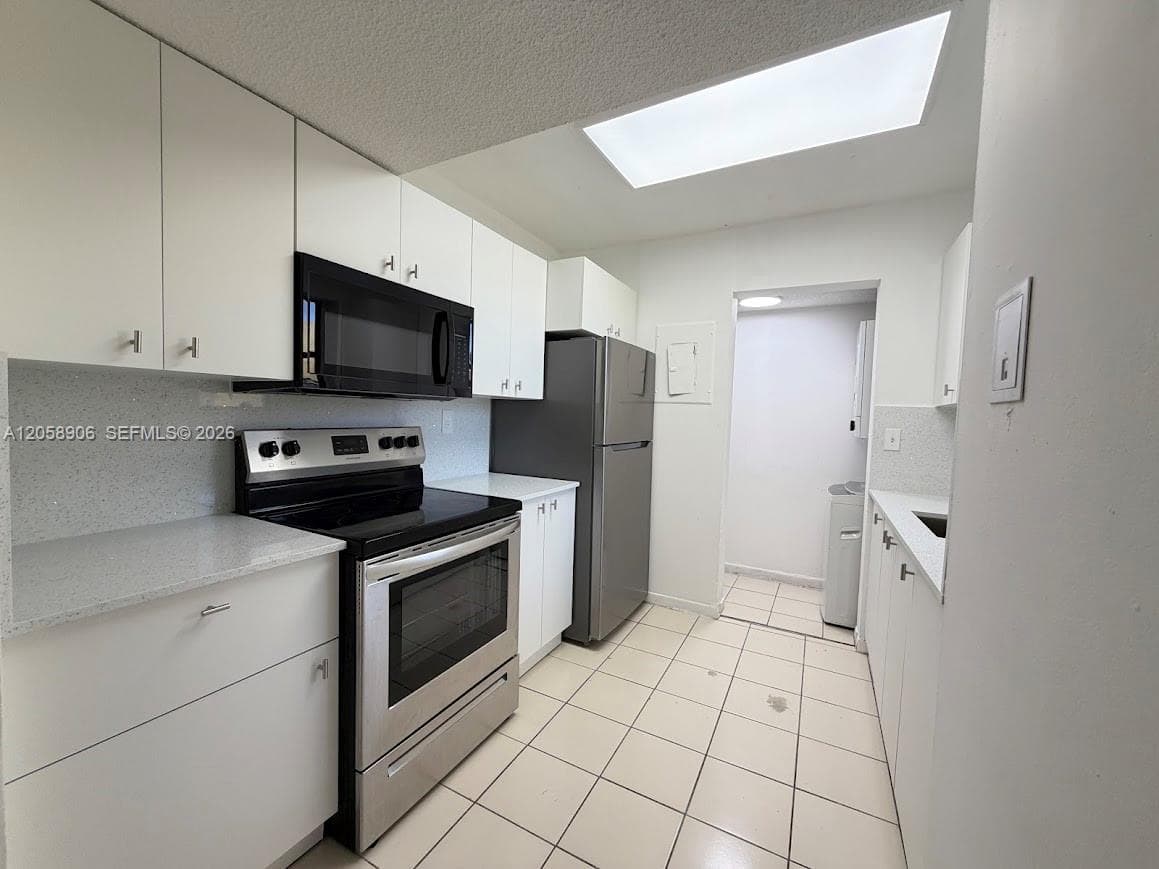 Kitchen featuring white flat-panel cabinetry, stainless steel appliances, speckled solid-surface countertops, ceramic tile flooring, and a recessed ceiling light fixture