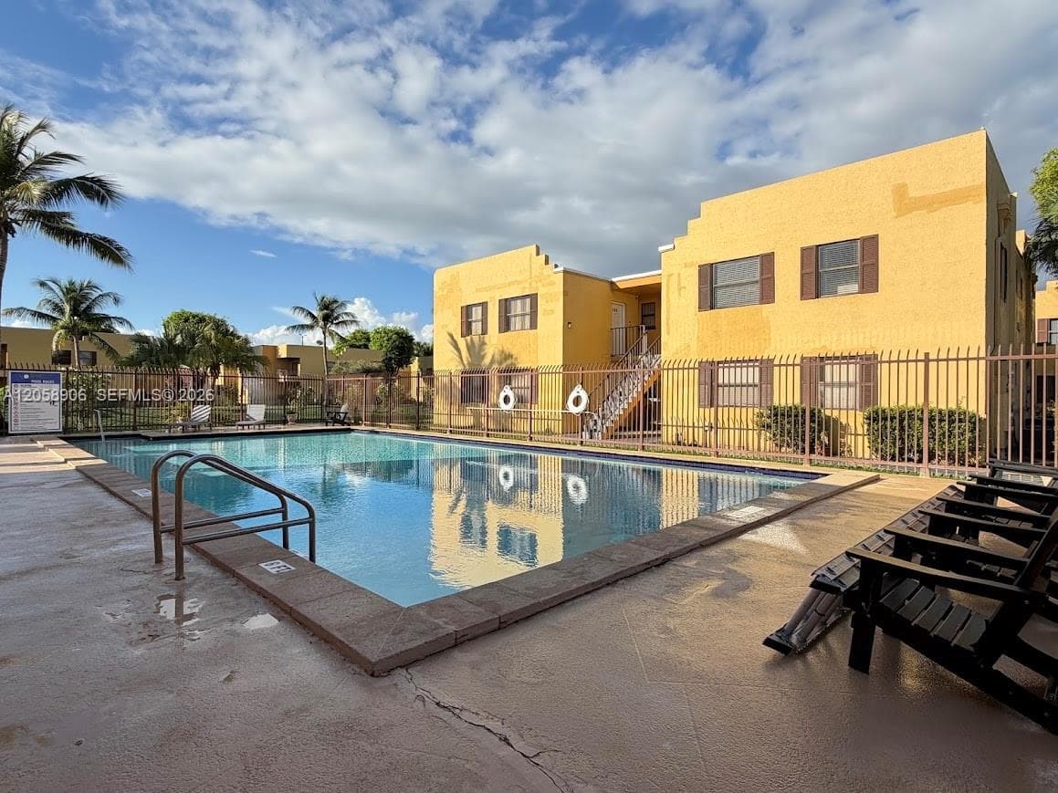 Rectangular swimming pool with metal handrails, concrete pool deck, and perimeter fencing