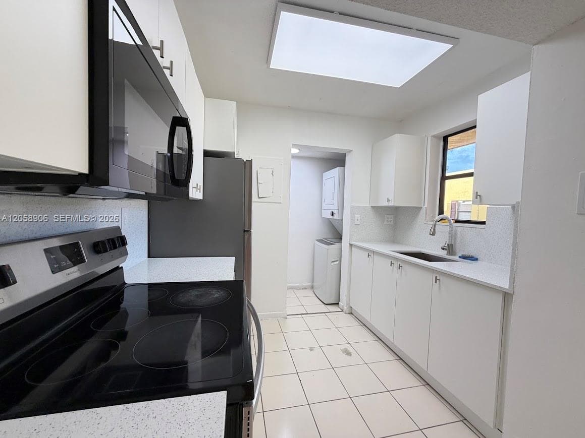 Kitchen featuring white cabinetry, solid-surface countertops, tile flooring, and integrated stainless steel and black appliances