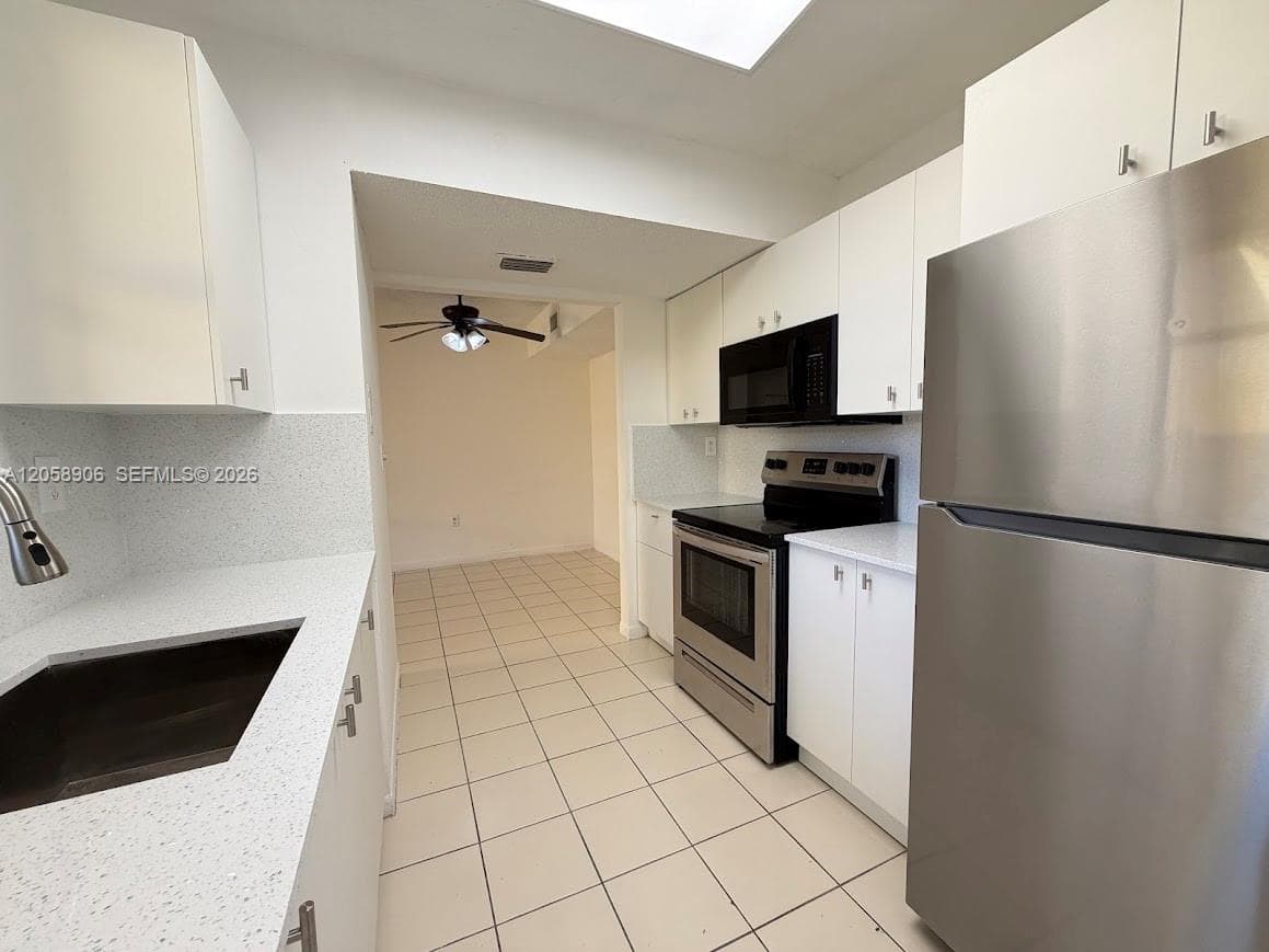 Kitchen featuring white cabinetry, solid-surface countertops, stainless steel appliances, and tile flooring