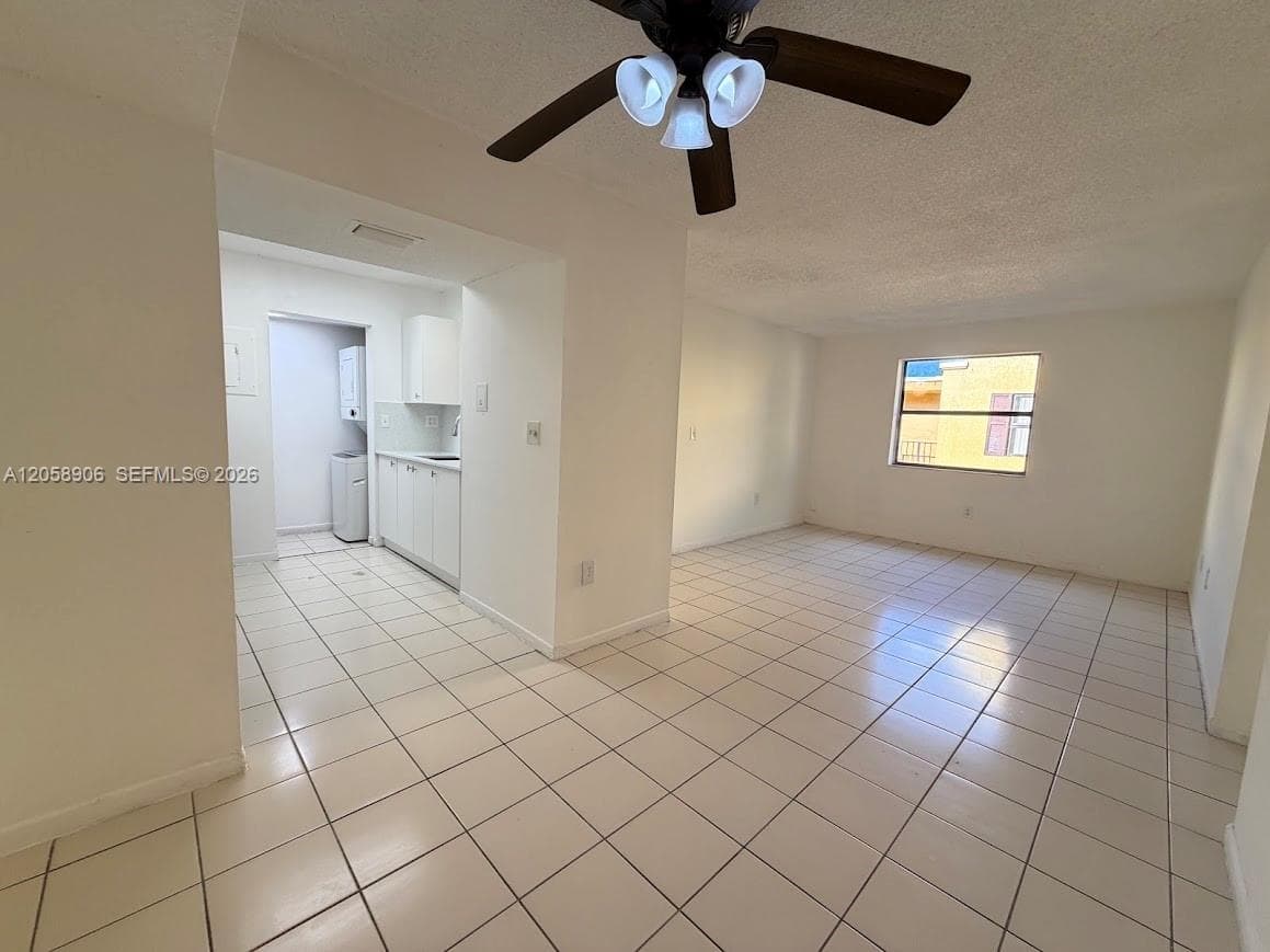 Open floor plan featuring tile flooring, ceiling fan with light fixture, and kitchen area with white cabinetry