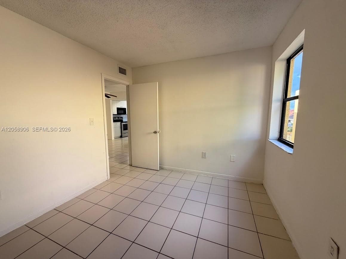 Neutral-toned interior space featuring light-colored square floor tiles and a single-pane window with dark framing