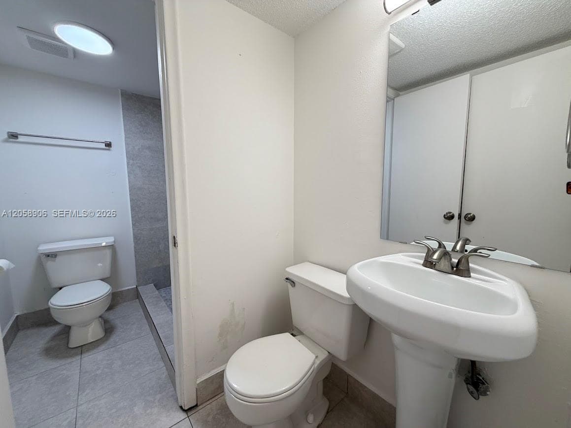 Bathroom featuring a pedestal sink with a metallic faucet, a wall-mounted mirror, a two-piece toilet, and tile flooring