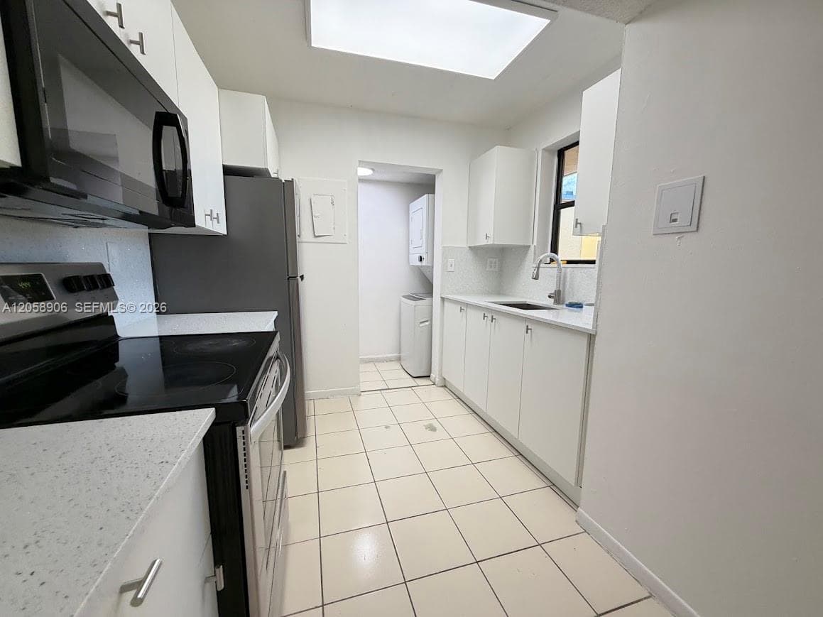 Kitchen featuring white cabinetry, quartz countertops, tile flooring, stainless steel appliances, and a dedicated laundry area