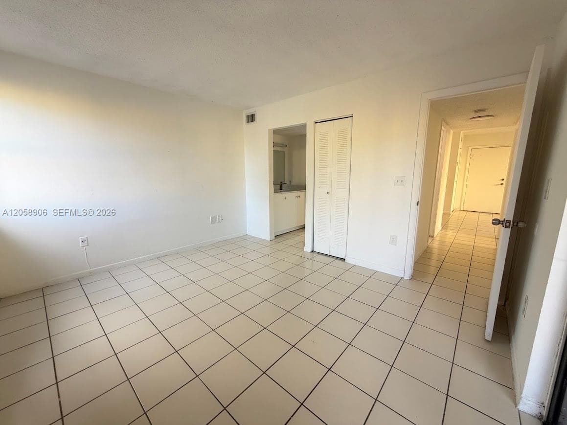 Room interior featuring neutral tile flooring, bi-fold closet doors, and recessed access to a vanity area