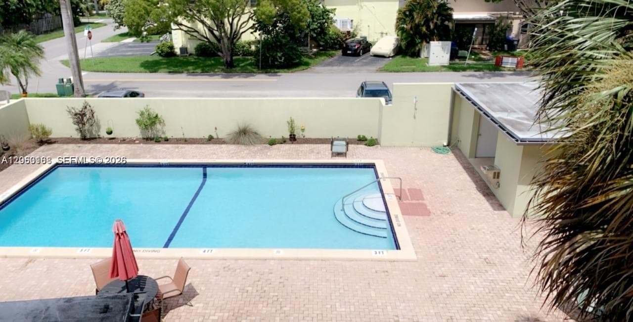 Rectangular swimming pool featuring integrated steps and stone-paver decking enclosed by a privacy wall