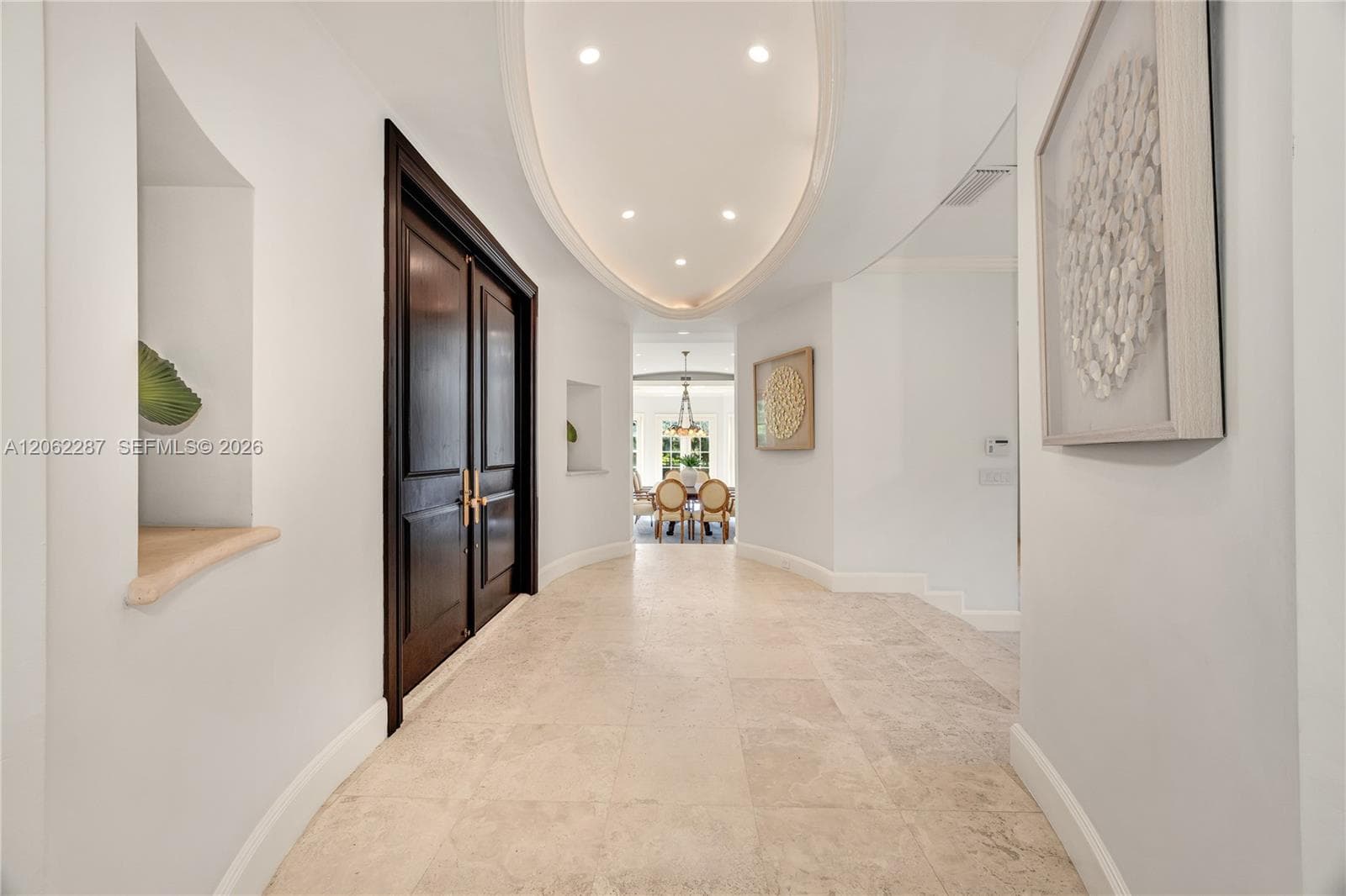 Foyer featuring stone tile flooring, double-door entry with brass hardware, oval tray ceiling with recessed lighting, and integrated wall niches