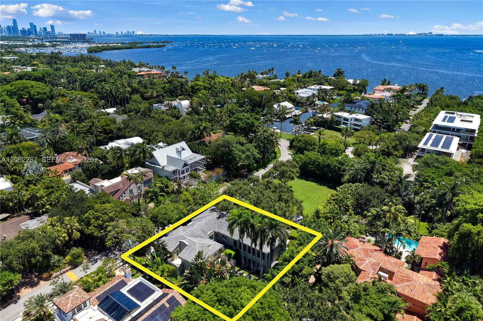 Aerial perspective of a multi-structure residence featuring a pitched roof, mature palms, dense landscaping, and expansive green space within the property boundaries
