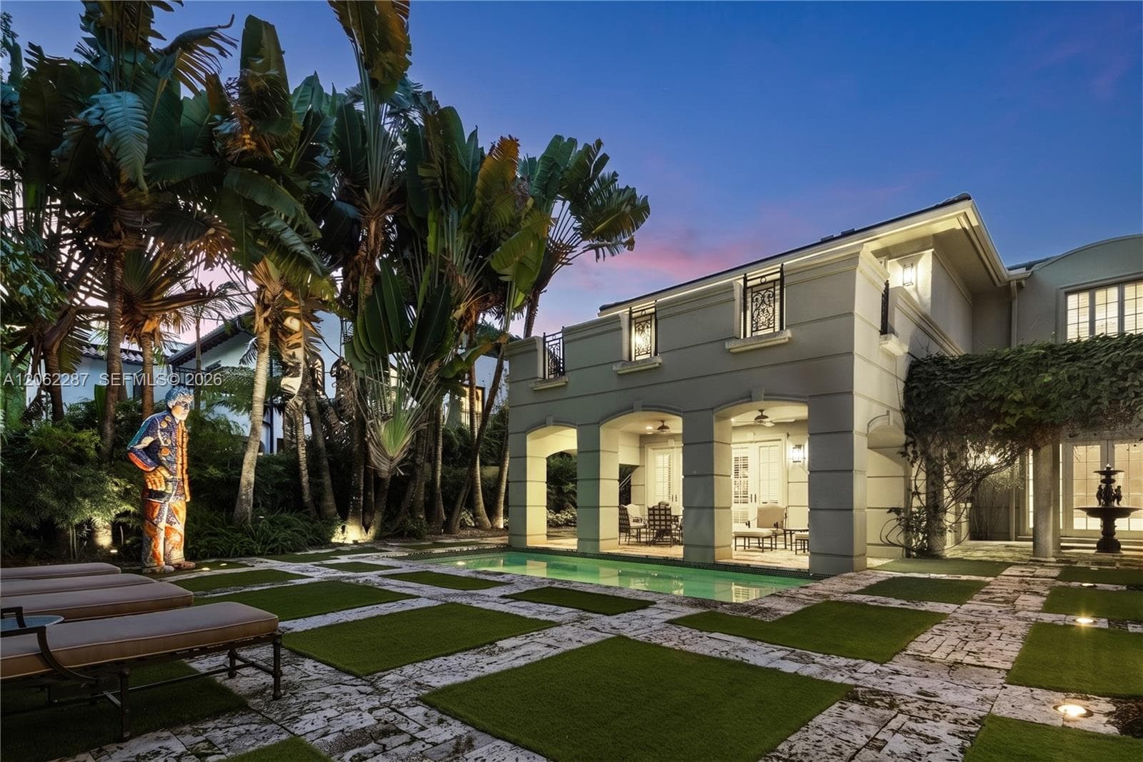 Covered loggia featuring arched architectural details, integrated swimming pool, structured paver and turf patio, and mature tropical landscaping