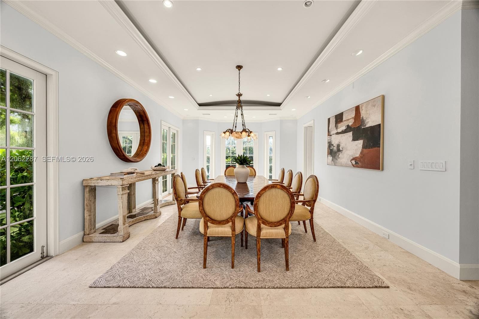 Tray ceiling with recessed lighting, stone flooring, multiple glass-paneled exterior doors, and a multi-arm chandelier