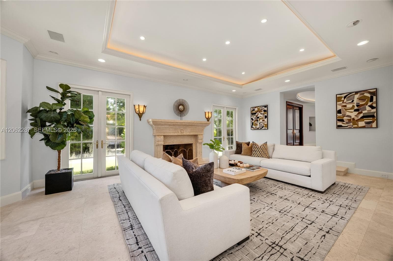 Tray ceiling with recessed lighting, carved stone fireplace surround, tile flooring, and dual sets of French doors with glass panes